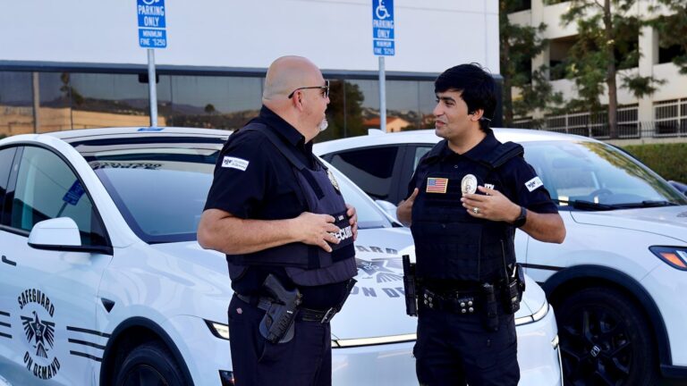 Two armed Safeguard On Demand officers talking beside a marked Tesla patrol car