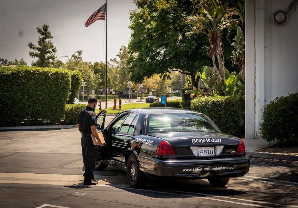 Safeguard On Demand security officer completing a daily activity report beside a marked patrol car in California