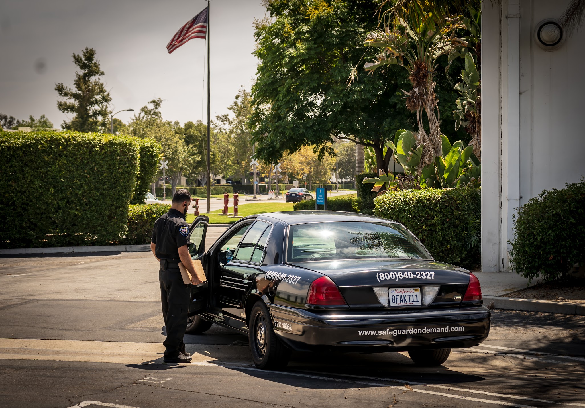 Safeguard On Demand security officer completing a daily activity report beside a marked patrol car in the Inland Empire