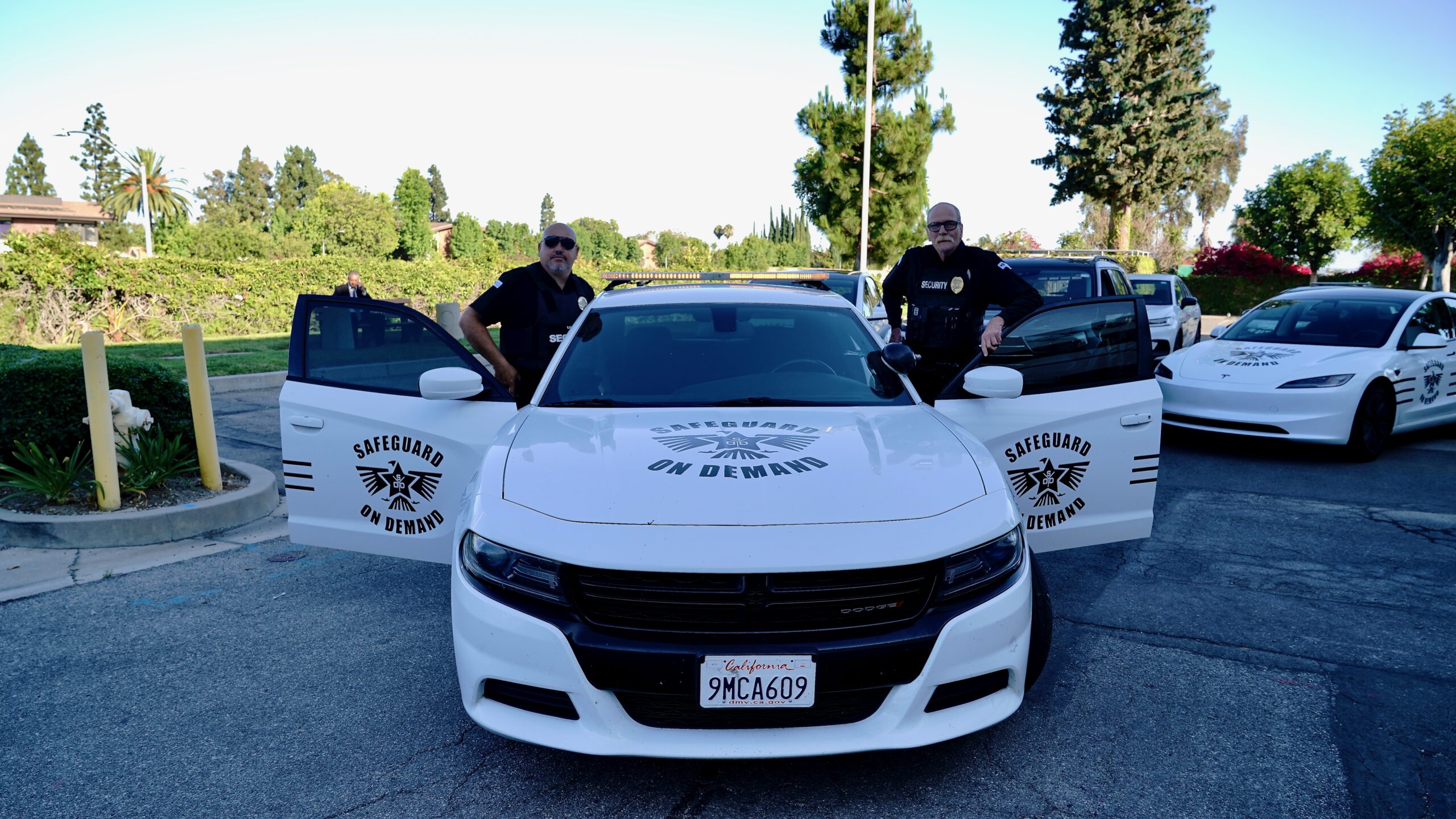 Safeguard On Demand armed security officers standing with a marked patrol car and Tesla patrol vehicle in Southern California